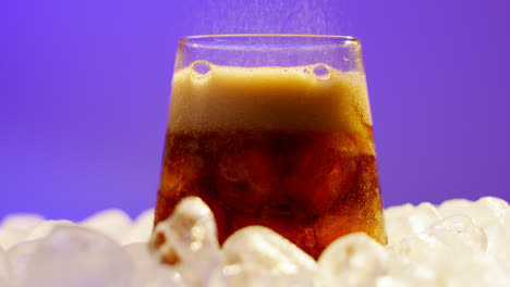 Nahaufnahme-Einer-Person,-Die-Gekühltes-Kaltgetränk-Aus-Der-Dose-Auf-Eiswürfel-Vor-Violettem-Hintergrund-In-Ein-Glas-Gießt